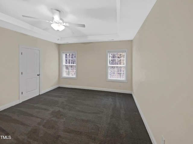 empty room with a tray ceiling, dark carpet, baseboards, and ceiling fan