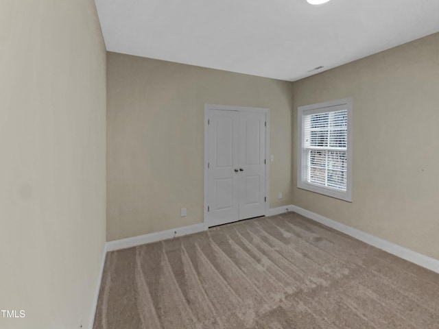 spare room featuring light colored carpet and baseboards