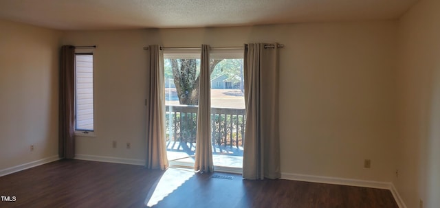 empty room featuring dark wood finished floors, a textured ceiling, and baseboards