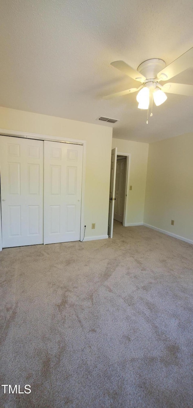 unfurnished bedroom featuring a textured ceiling, light colored carpet, a ceiling fan, baseboards, and visible vents