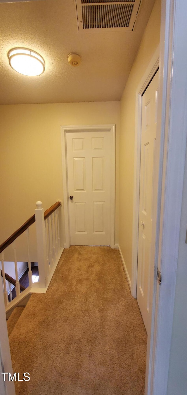 hall with visible vents, carpet flooring, a textured ceiling, an upstairs landing, and baseboards