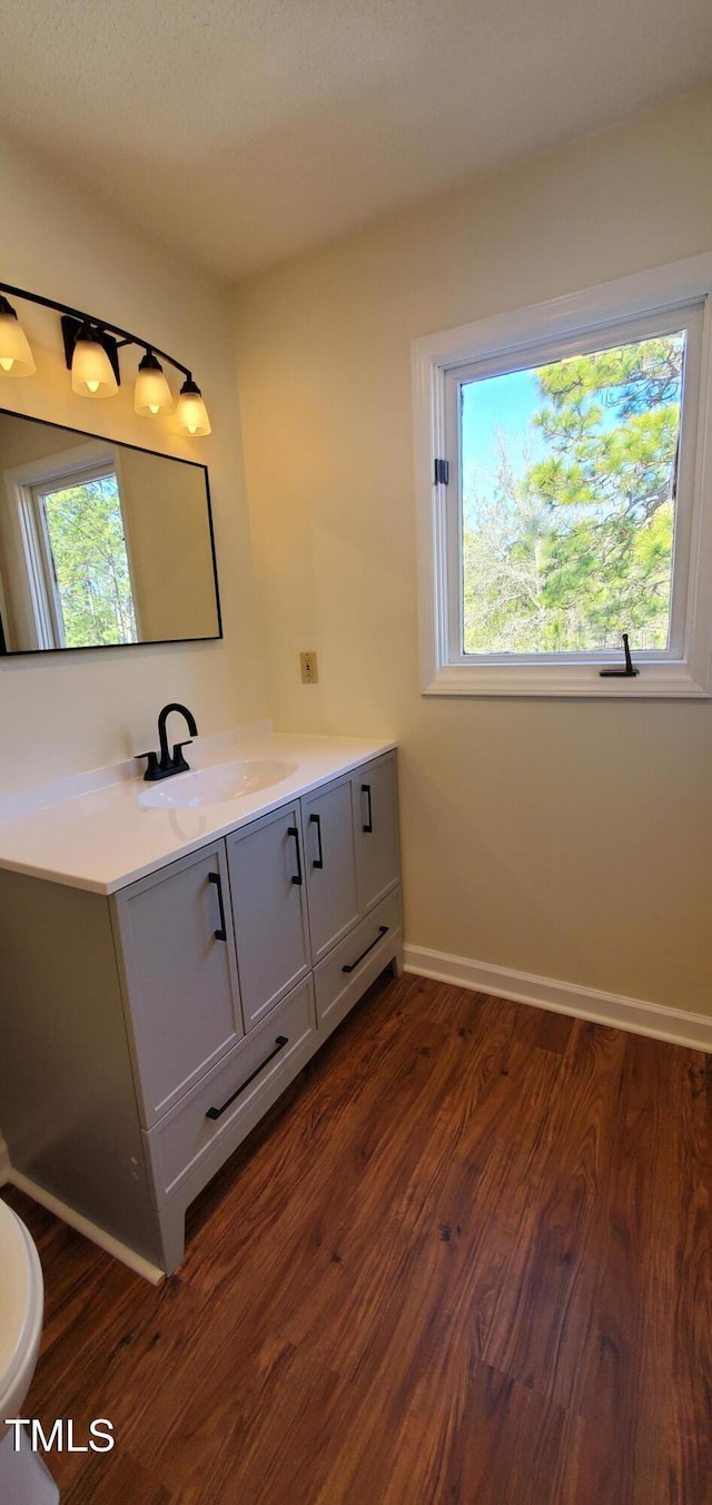 bathroom featuring toilet, baseboards, wood finished floors, and vanity