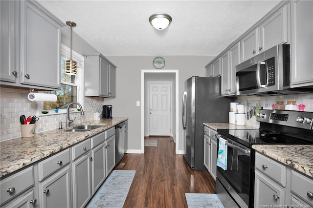 kitchen with dark wood finished floors, hanging light fixtures, gray cabinets, stainless steel appliances, and a sink