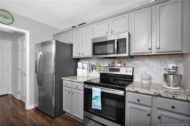 kitchen featuring gray cabinetry, stainless steel appliances, light stone countertops, tasteful backsplash, and dark wood finished floors