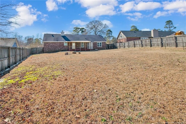 rear view of property with a yard, brick siding, a chimney, and a fenced backyard