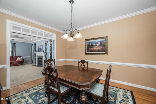 dining room featuring wood finished floors, ornamental molding, a fireplace with flush hearth, and baseboards