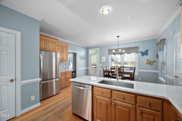 kitchen featuring light wood finished floors, stainless steel appliances, hanging light fixtures, brown cabinetry, and a sink