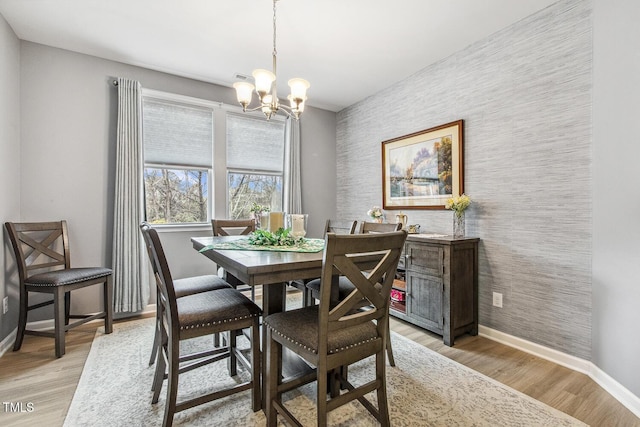 dining space featuring light wood-style floors, wallpapered walls, baseboards, and an inviting chandelier