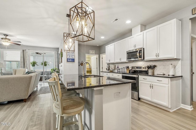 kitchen featuring tasteful backsplash, open floor plan, stainless steel appliances, light wood-type flooring, and a sink