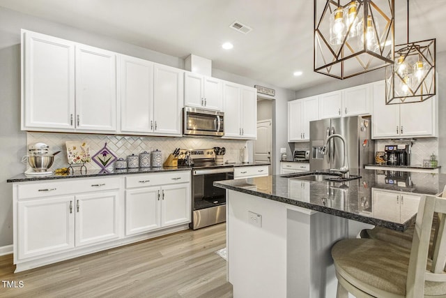 kitchen with visible vents, white cabinets, dark stone counters, stainless steel appliances, and light wood-type flooring