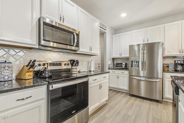 kitchen with stainless steel appliances, white cabinetry, light wood-type flooring, decorative backsplash, and dark stone countertops