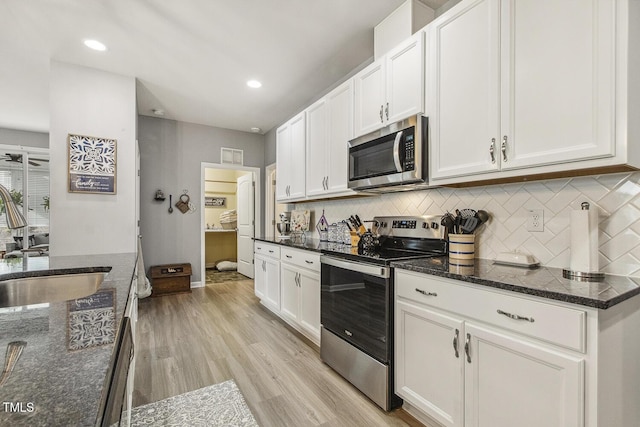 kitchen with stainless steel appliances, light wood-style flooring, decorative backsplash, white cabinets, and a sink