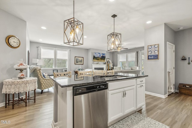 kitchen featuring light wood finished floors, dishwasher, open floor plan, dark stone countertops, and a sink