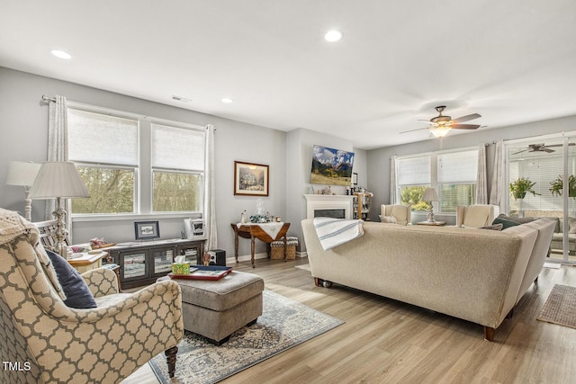 living area with a fireplace, recessed lighting, light wood-style flooring, a ceiling fan, and baseboards