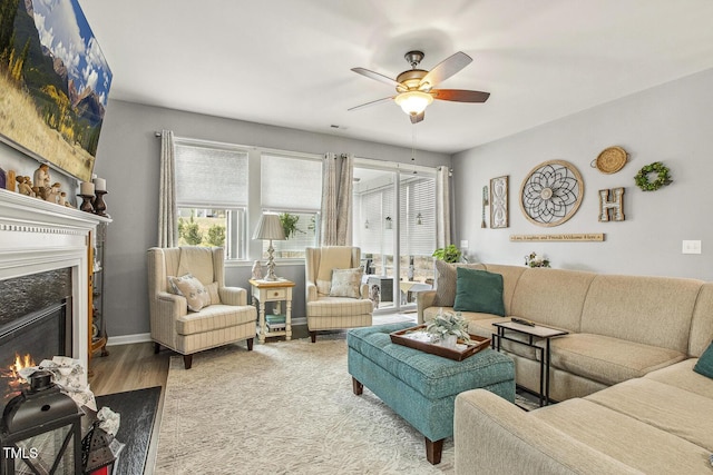 living area featuring a lit fireplace, baseboards, ceiling fan, and wood finished floors