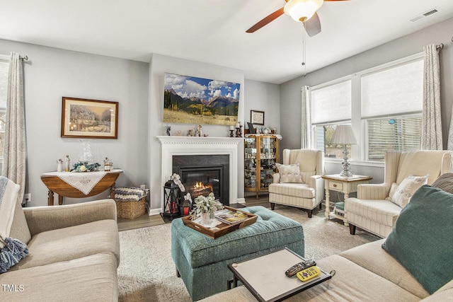 living area featuring baseboards, visible vents, a glass covered fireplace, ceiling fan, and wood finished floors