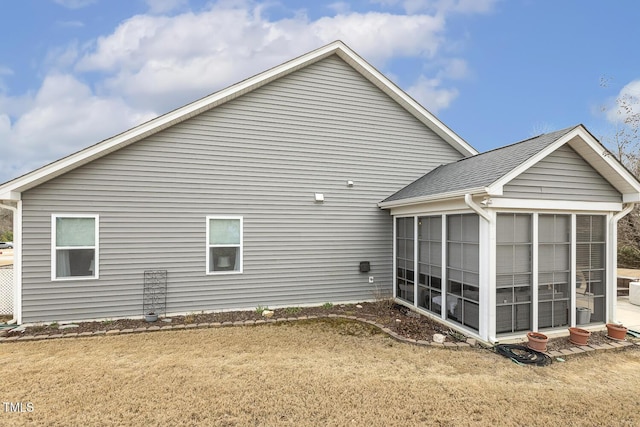 rear view of property with a lawn, roof with shingles, and a sunroom