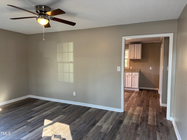 empty room featuring dark wood-type flooring, ceiling fan, and baseboards