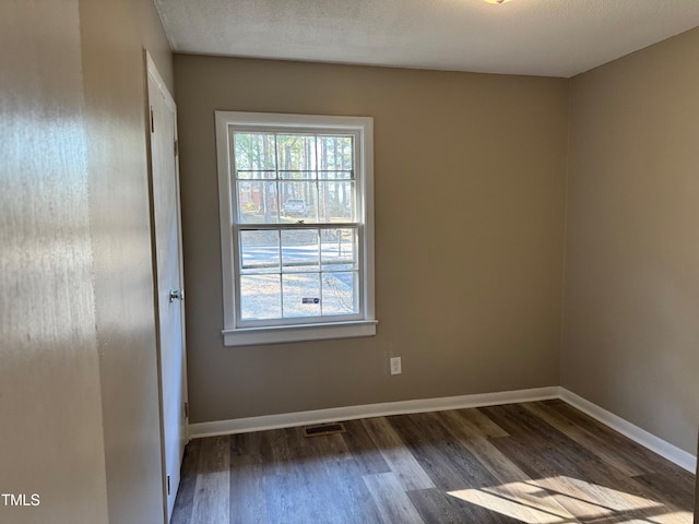 unfurnished room with visible vents, a textured ceiling, baseboards, and dark wood-type flooring