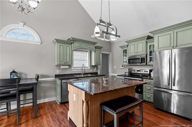 kitchen with a sink, appliances with stainless steel finishes, a center island, glass insert cabinets, and an inviting chandelier