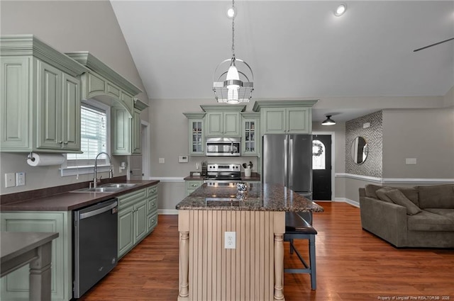 kitchen featuring stainless steel appliances, a sink, open floor plan, a center island, and glass insert cabinets