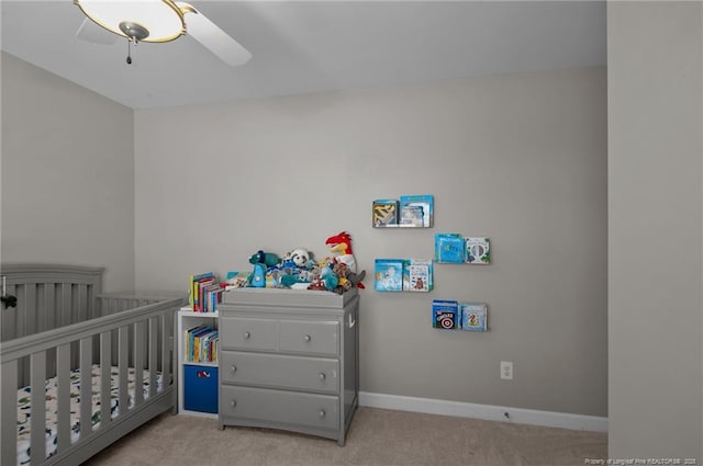 bedroom with light carpet, ceiling fan, a crib, and baseboards