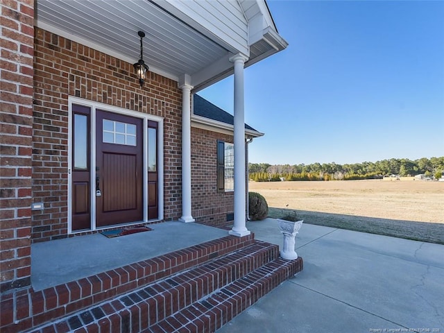 view of exterior entry featuring brick siding and a porch