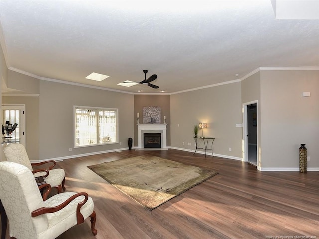 living area featuring dark wood finished floors, a fireplace, a ceiling fan, ornamental molding, and baseboards