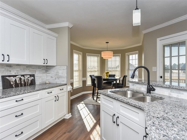 kitchen with decorative light fixtures, decorative backsplash, white cabinets, a sink, and light stone countertops