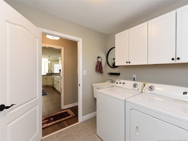 laundry room with cabinet space, light tile patterned floors, baseboards, washing machine and dryer, and a sink