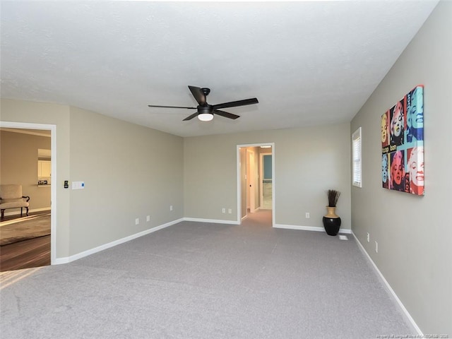 carpeted spare room with a ceiling fan and baseboards