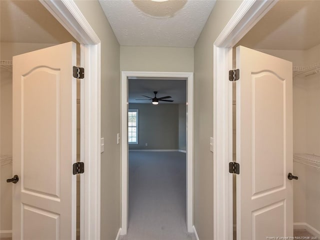 hall with carpet floors, a textured ceiling, and baseboards