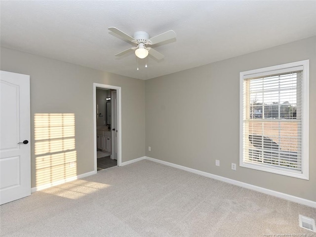 unfurnished bedroom featuring light colored carpet, a ceiling fan, baseboards, visible vents, and ensuite bath