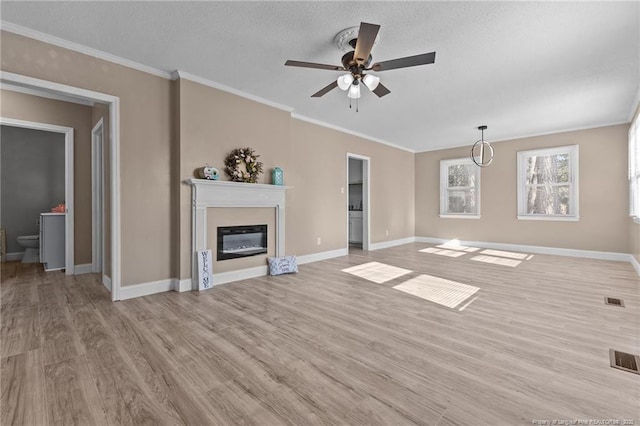 unfurnished living room featuring crown molding, visible vents, light wood-style flooring, a glass covered fireplace, and baseboards