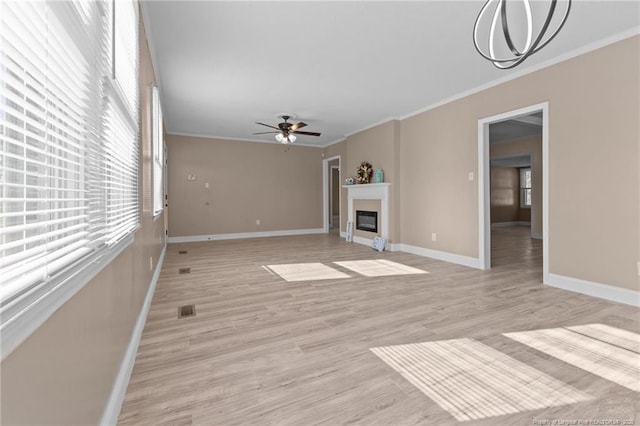 unfurnished living room with plenty of natural light, a ceiling fan, crown molding, and a glass covered fireplace