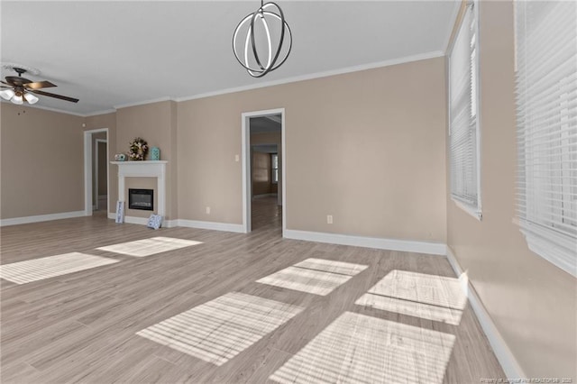 unfurnished living room featuring ornamental molding, a glass covered fireplace, baseboards, and light wood finished floors