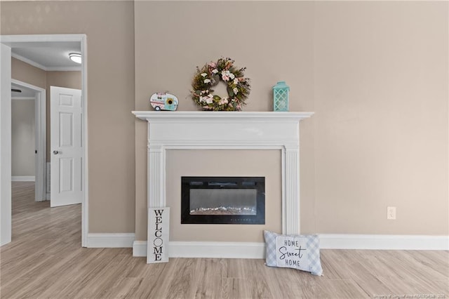 interior details with crown molding, wood finished floors, a glass covered fireplace, and baseboards