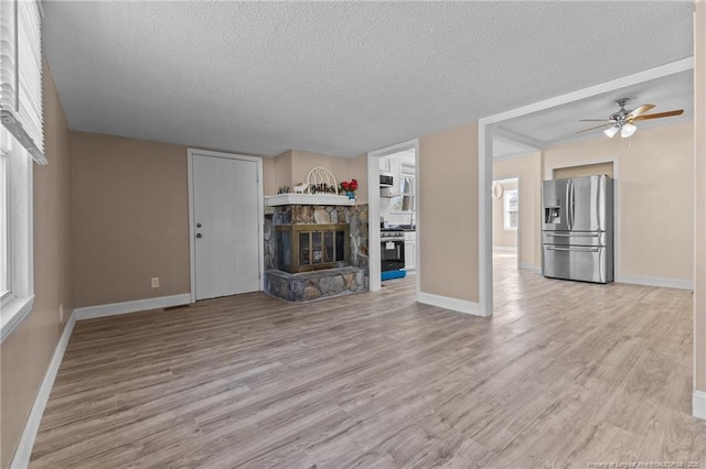 unfurnished living room featuring light wood-type flooring, baseboards, a textured ceiling, and a stone fireplace