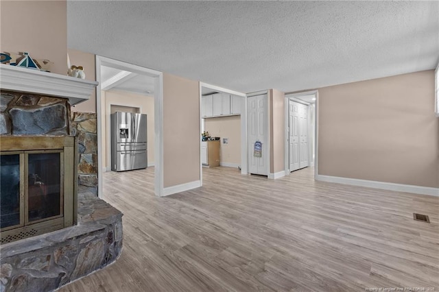 living room with a textured ceiling, light wood-style flooring, a fireplace, visible vents, and baseboards