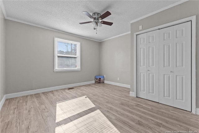 unfurnished bedroom featuring crown molding, light wood finished floors, a closet, a textured ceiling, and baseboards