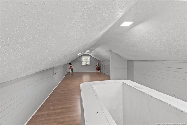 bonus room featuring vaulted ceiling, a textured ceiling, dark wood finished floors, and wooden walls