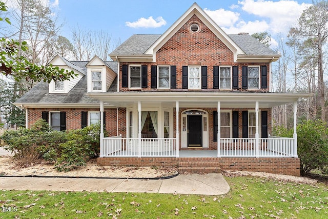 view of front of property featuring covered porch, brick siding, and roof with shingles