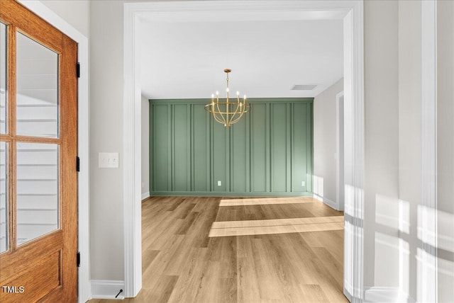 unfurnished dining area with visible vents, light wood-style flooring, baseboards, and an inviting chandelier