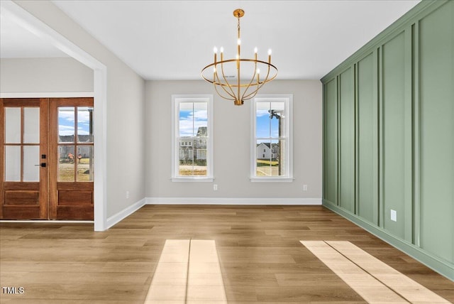 unfurnished dining area with french doors, baseboards, light wood finished floors, and an inviting chandelier