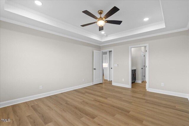 unfurnished bedroom with baseboards, light wood-style flooring, ornamental molding, a tray ceiling, and recessed lighting