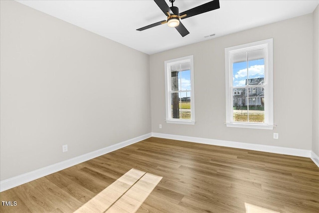 unfurnished room with visible vents, wood finished floors, a ceiling fan, and baseboards