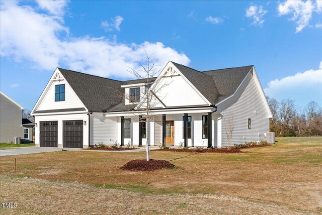 modern farmhouse with driveway, a garage, covered porch, cooling unit, and a front lawn