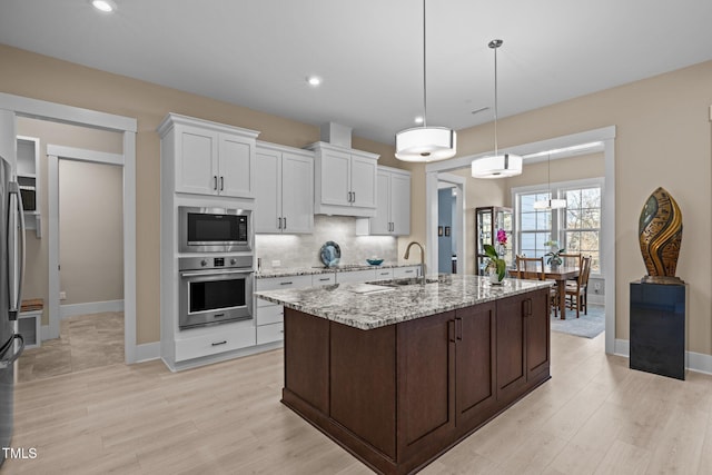 kitchen featuring stainless steel appliances, a sink, white cabinetry, light stone countertops, and tasteful backsplash