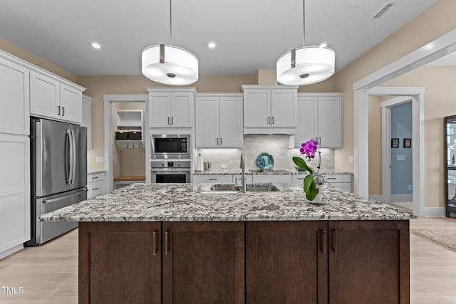 kitchen featuring light wood finished floors, stainless steel appliances, decorative backsplash, white cabinets, and a sink