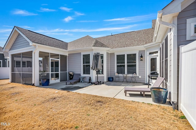 back of house with a shingled roof, a sunroom, a patio, and a lawn